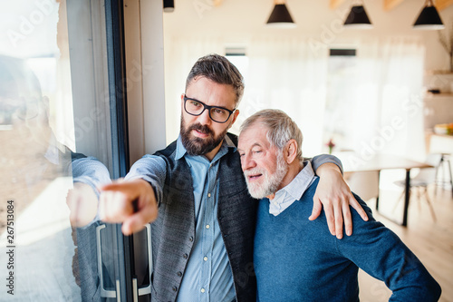 A portrait of adult hipster son and senior father indoors at home, talking. photo