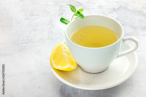 A cup of green tea with a wedge of lemon and mint leaves, with a place for text