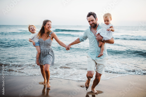Young family with two toddler children walking on beach on summer holiday.