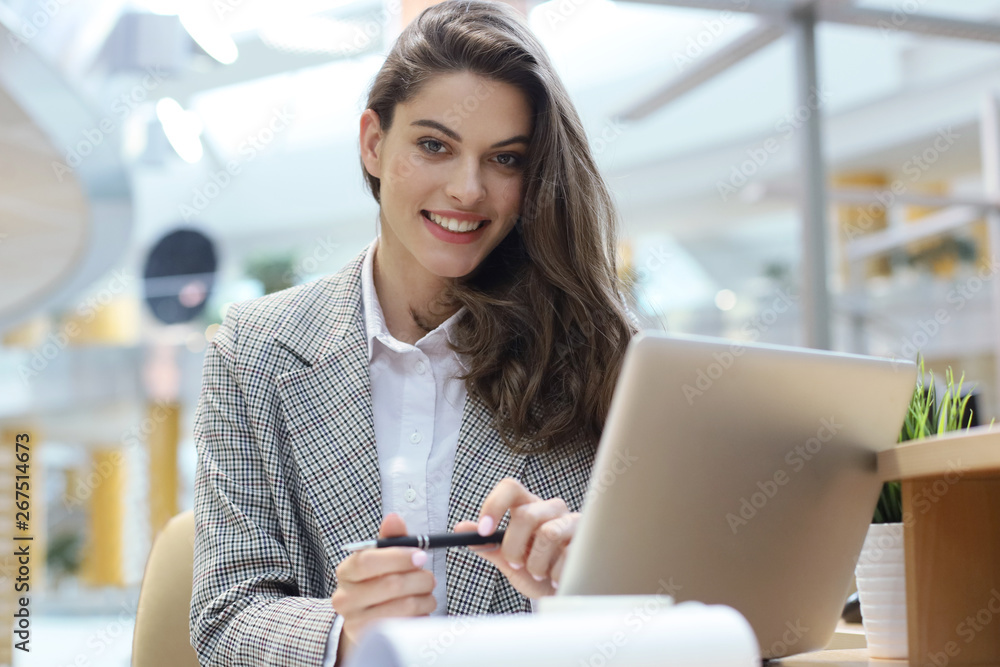Portrait of a cheerful young businesswoman sitting at the table in office and looking at camera. Portrait of a cheerful young businesswoman sitting at the table in office and looking at camera.