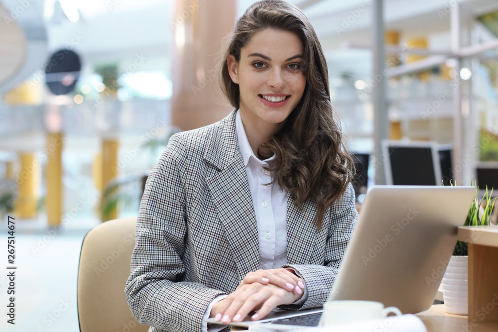 Portrait of a cheerful young businesswoman sitting at the table in office and looking at camera. Portrait of a cheerful young businesswoman sitting at the table in office and looking at camera.