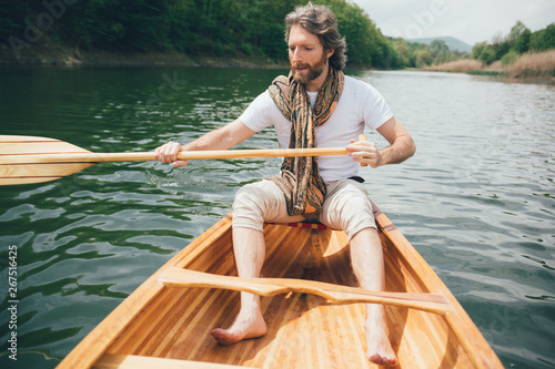 Casual dressed bearded man paddling a canoe on water