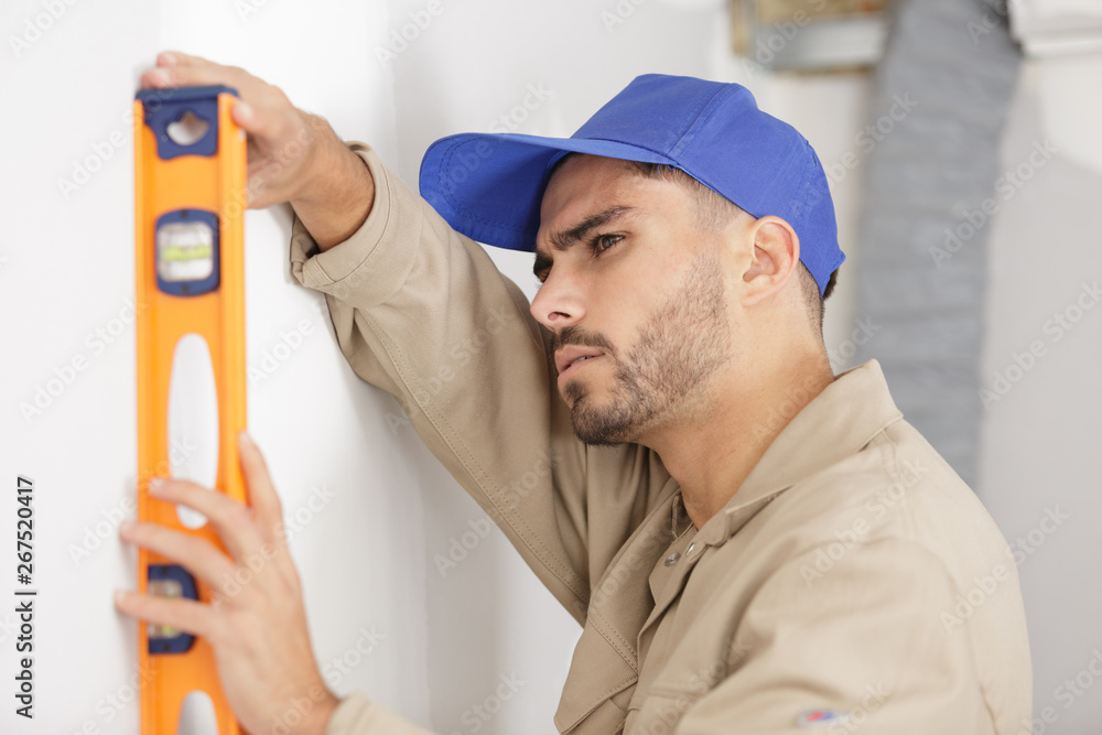 young tradesman using a spirit level on wall young tradesman using a spirit level on wall