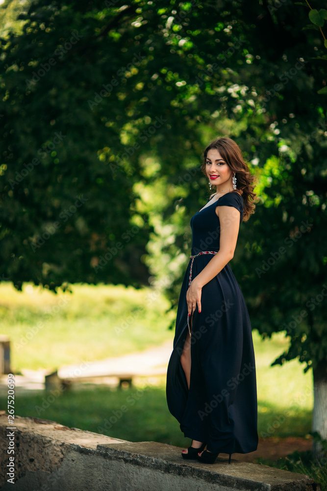 Gorgeous woman in dark blue dress stand in front of green background in the park Gorgeous woman in dark blue dress stand in front of green background in the park