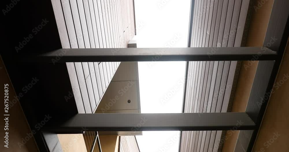 Modern building architecture camera tilt from the sky downwards in an alley or patio. Brown structure with a blacony off to the side for a very modern environment. Shot in showmotion 4k.mov