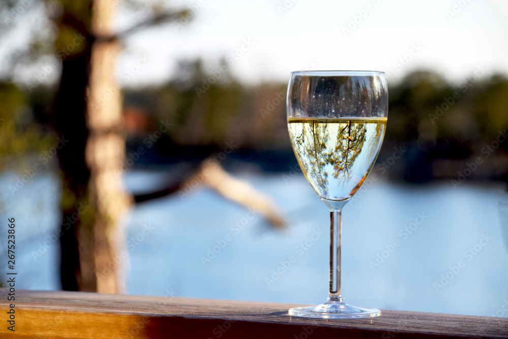 Glass of white wine on wooden deck railing with a beautiful view of the sea in the background on a summer evening in Sweden Glass of white wine on wooden deck railing with a beautiful view of the sea in the background on a summer evening in Sweden