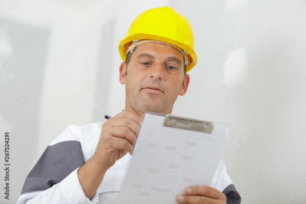 workman writing on clipboard looking sceptical workman writing on clipboard looking sceptical