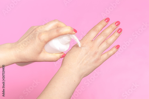 woman applying cream on hands on pink background