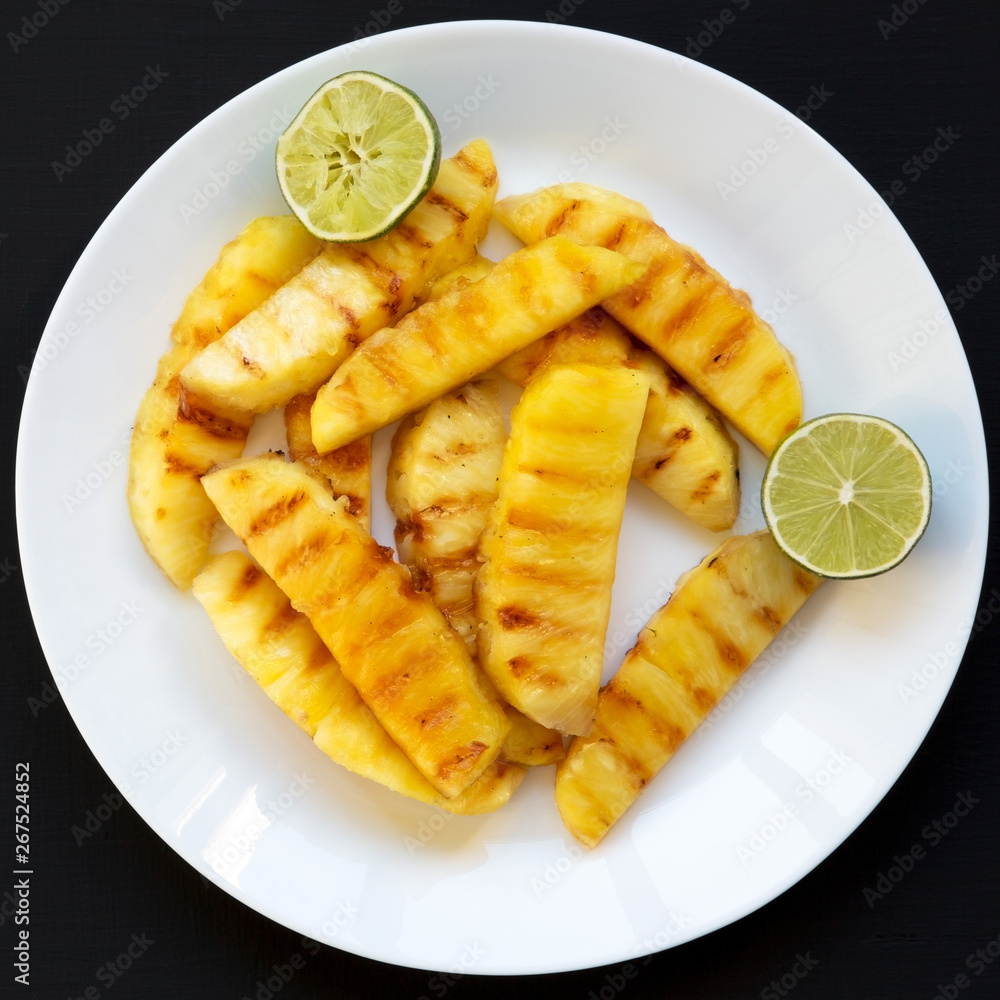 Grilled pineapple wedges on a white plate over black surface. Summer food. Close-up. Grilled pineapple wedges on a white plate over black surface. Summer food. Close-up.