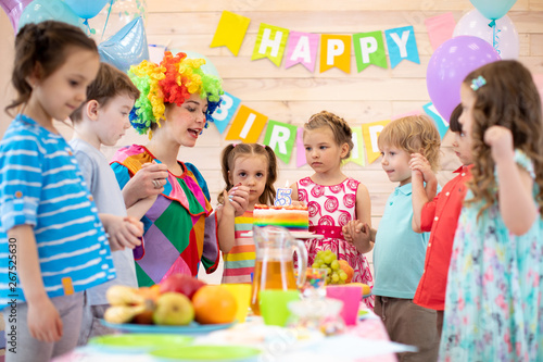 Children group with clown celebrating birthday party in daycare. Happy kids hold each other's hands