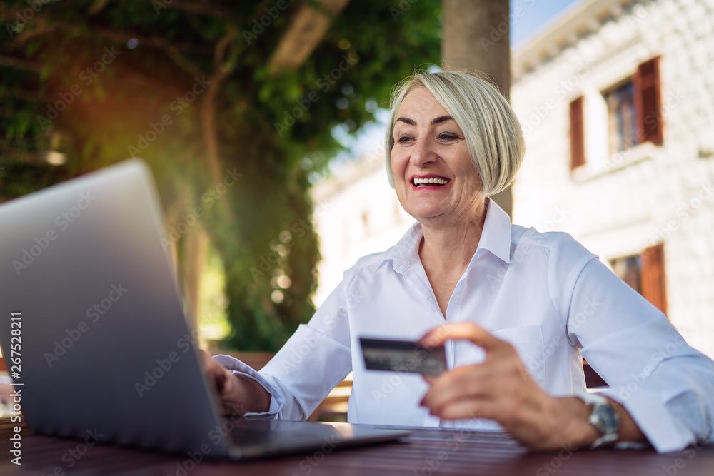 Happy mature woman sitting at a cafe and using laptop for shopping online with credit card Happy mature woman sitting at a cafe and using laptop for shopping online with credit card