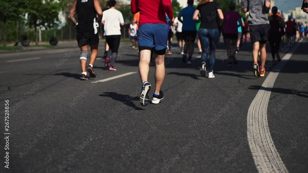 Participants of the marathon run along the road on a city street on a sunny spring day. Slow motion. Legs close-up. Sport and healthy lifestyle. Run at the marathon Participants of the marathon run along the road on a city street on a sunny spring day. Slow motion. Legs close-up. Sport and healthy lifestyle. Run at the marathon