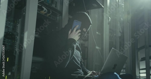 Hacker in black mask with laptop talking smartphone stops cyberattack and runs away. Cyberattack and data security concept. photo