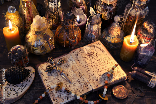 Ancient witch book with magic spell, black candles and decorated bottles.
