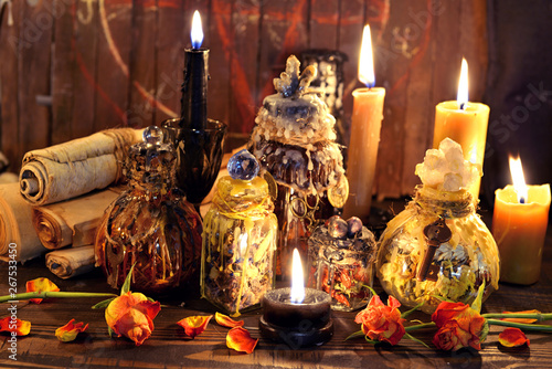 Witch bottles, black candles and roses agains planks with pentagram.