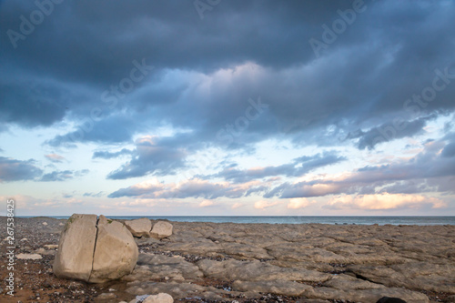 Rocks on a Sussex beach at low tide, with ominous clouds overhead © lemanieh