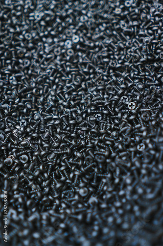 Many black small screws for repair and fasteners in a box close-up.