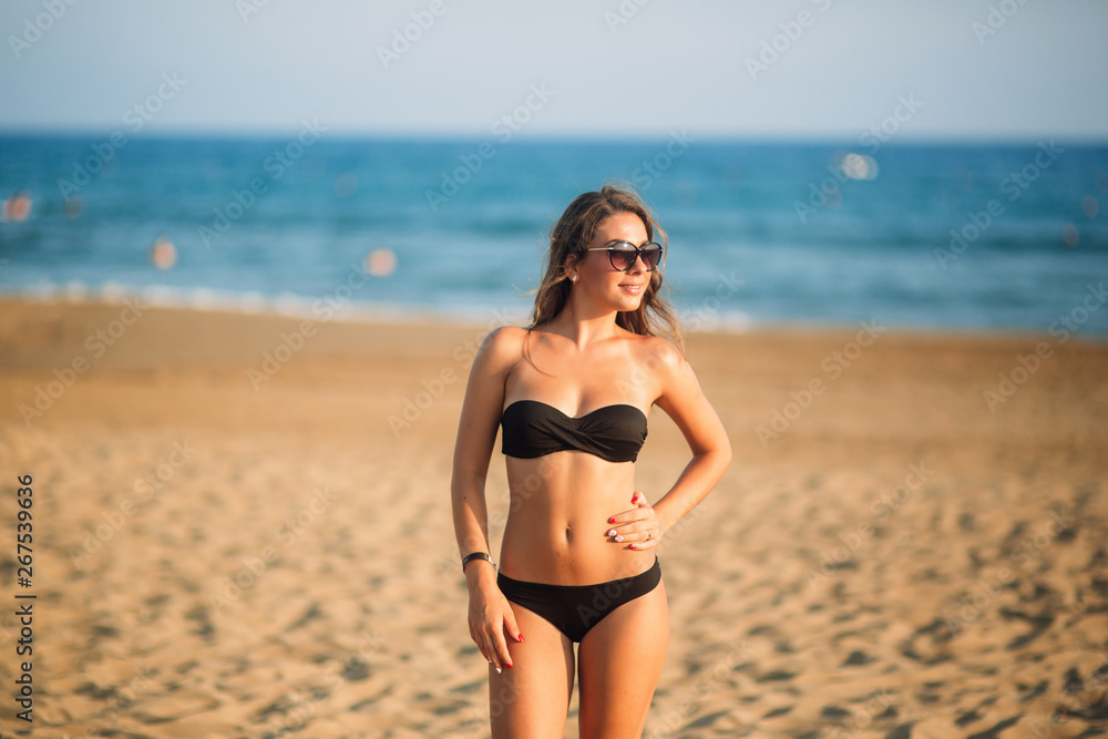 Sexy lady in bikini sunbathing on a sandy beach. Fashion model on the coast in sunset