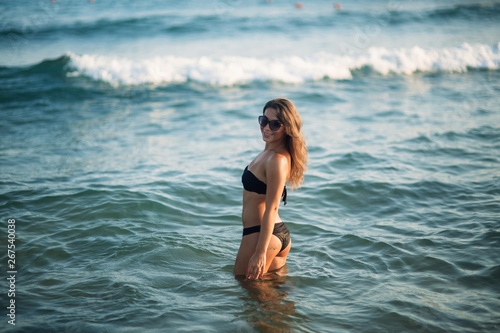 Beautiful lady is waist-deep in the sea. Sexy woman in black bikini wait for waves in the sea © Aleksandr
