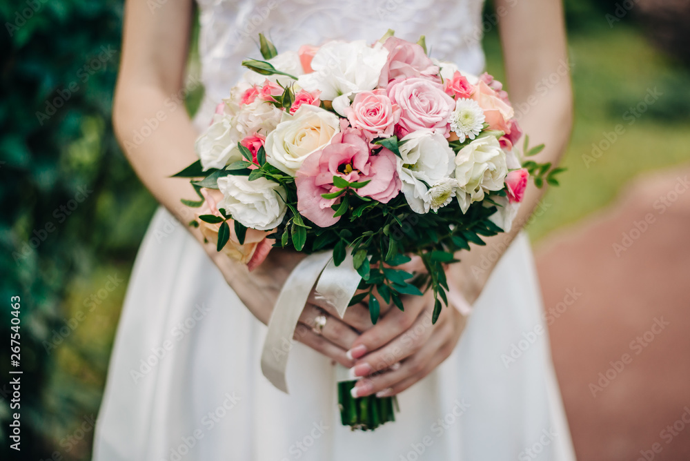bouquet of wedding flowers in the hands of the bride in a white long dress