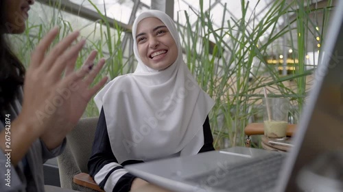 muslim woman and friend discussing with laptop. student learning in cafe