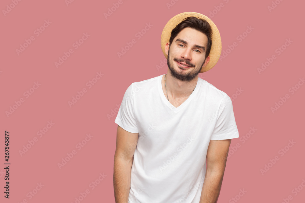 Portrait of happy bearded young man in white shirt with hat standing and looking at camera with smile. indoor studio shot, isolated on pink background copyspace. Portrait of happy bearded young man in white shirt with hat standing and looking at camera with smile. indoor studio shot, isolated on pink background copyspace.