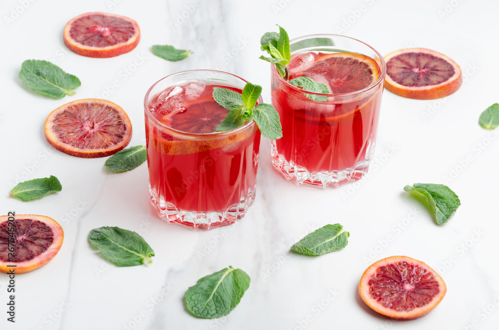 Two glasses of blood orange margarite and mint leaves, slices of blood orange on the white table Two glasses of blood orange margarite and mint leaves, slices of blood orange on the white table
