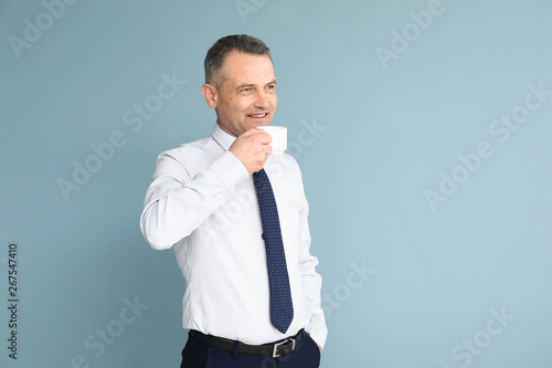 Handsome mature businessman drinking coffee on color background