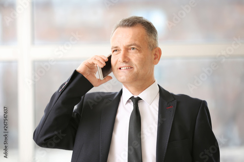 Handsome mature businessman talking by phone in office