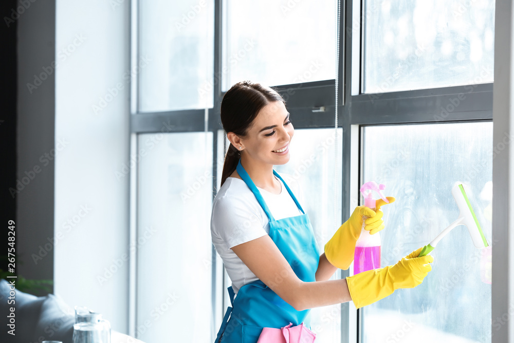 Female janitor cleaning window in office - obrazy, fototapety, plakaty 
