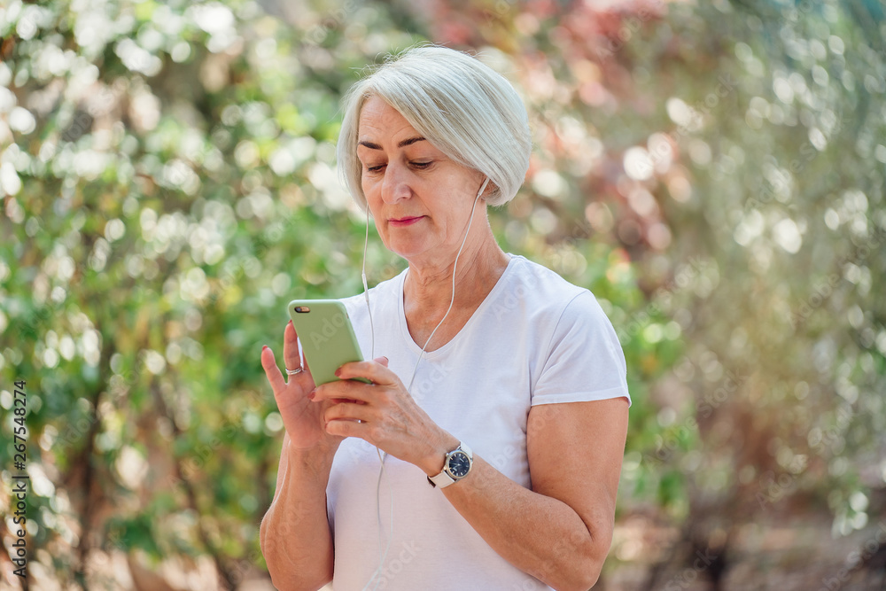 Senior woman runner in park using smartphone and earphones Senior woman runner in park using smartphone and earphones