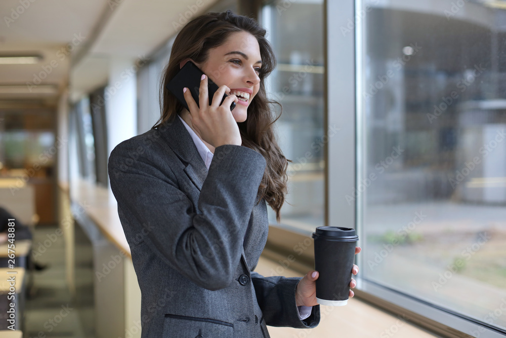 Young smiling business woman using smartphone near computer in office. Young smiling business woman using smartphone near computer in office.