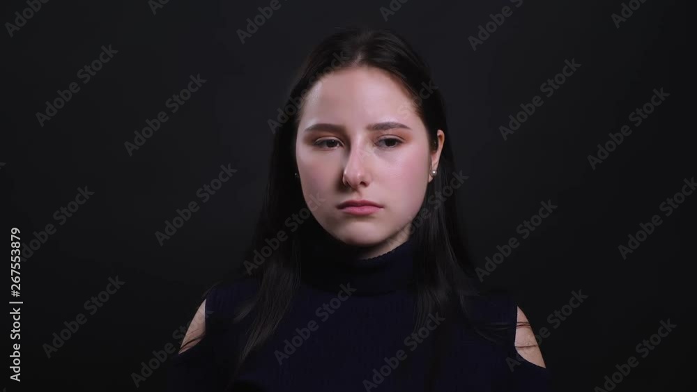 Closeup portrait of young attractive brunette female being sad and upset looking at camera with background isolated on black Closeup portrait of young attractive brunette female being sad and upset looking at camera with background isolated on black