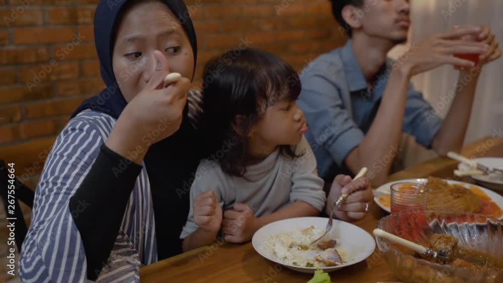 asian muslim mom eat with her daughter sitting on lap during dinner asian muslim mom eat with her daughter sitting on lap during dinner