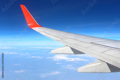 Airplane flying on blue sky and white cloud. Wing of an airplane flying above the cloud looks from the window of the plane. 