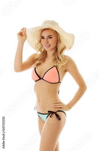 Young blond woman is posing in bikini and summer hat on white background.