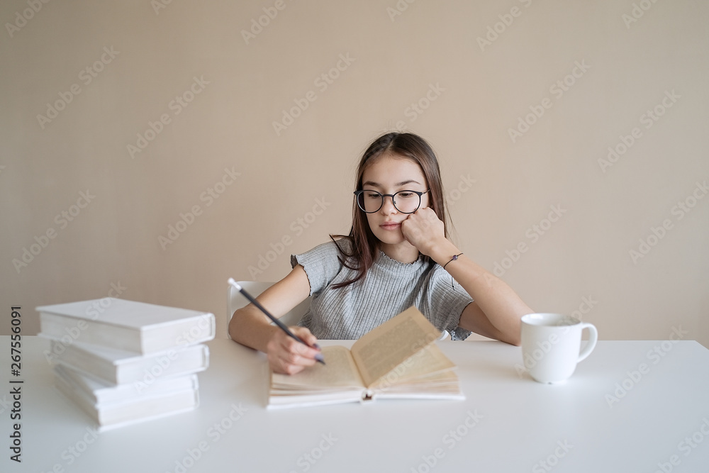 Cute teenager girl sitting at table with books and doing homework. Education, children and school concept Cute teenager girl sitting at table with books and doing homework. Education, children and school concept