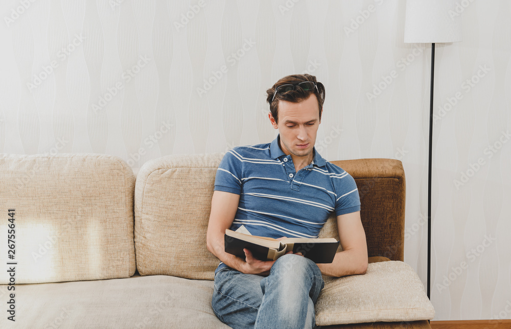 Casual man sitting on sofa and reading book in leisure time in home.
