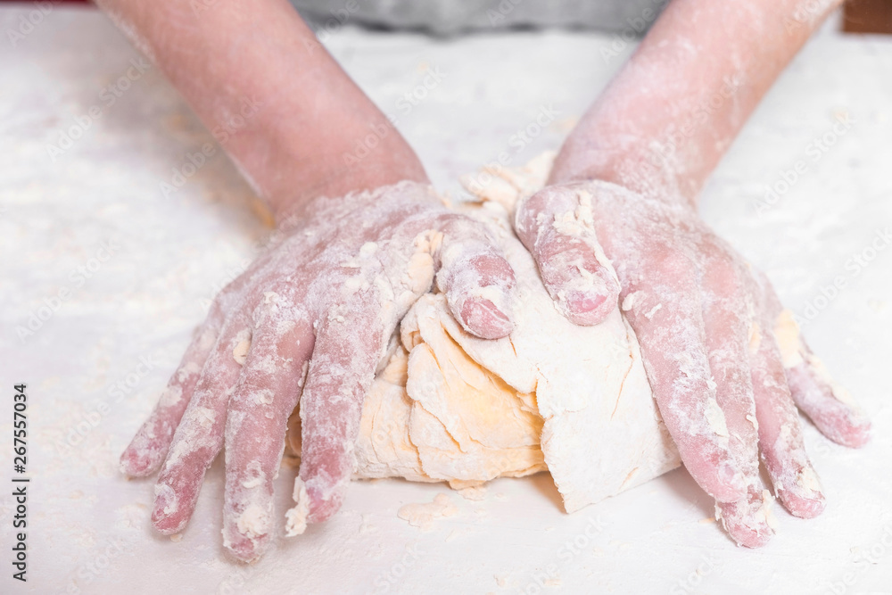 Boy preparing dough for baking on a white table close-up. There's a lot of flour on the table. Hands of the child in the cooking process Boy preparing dough for baking on a white table close-up. There's a lot of flour on the table. Hands of the child in the cooking process