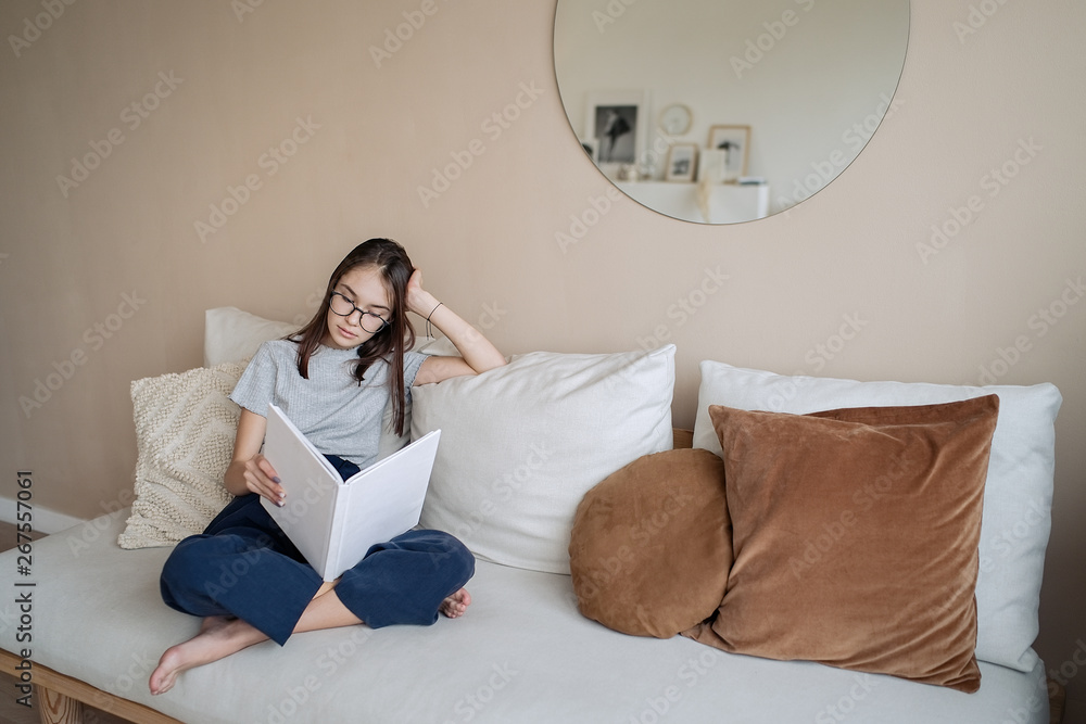 Cute teenager girl sitting on sofa at home with books and doing homework. Education, children and school concept, distance learning, self education     
