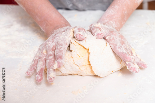 Teen prepares dough for baking on white table close up. There's a lot of flour on the table. Hands of the child in the cooking process