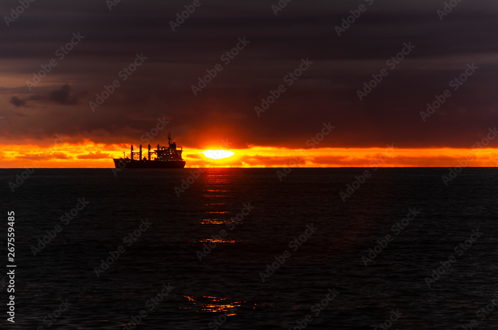 silhouette of the ship at sunset. the outline of a fishing barge against the setting sun. copyspace. moonlight path. orange sky