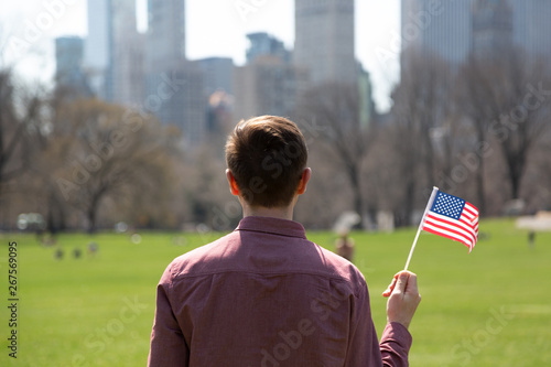Young man holding American flag and looking at skyscrapers from Central Park, New York City