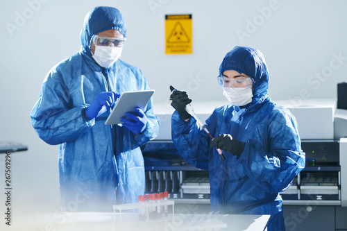 Serious concentrated multiethnic clinical scientists in biohazard suits and masks working with blood samples while doing research in laboratory
