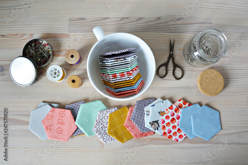 Hexagon english paper piecing templates, white cup, thread, retro scissors, metal pins and glass jar on the wooden table