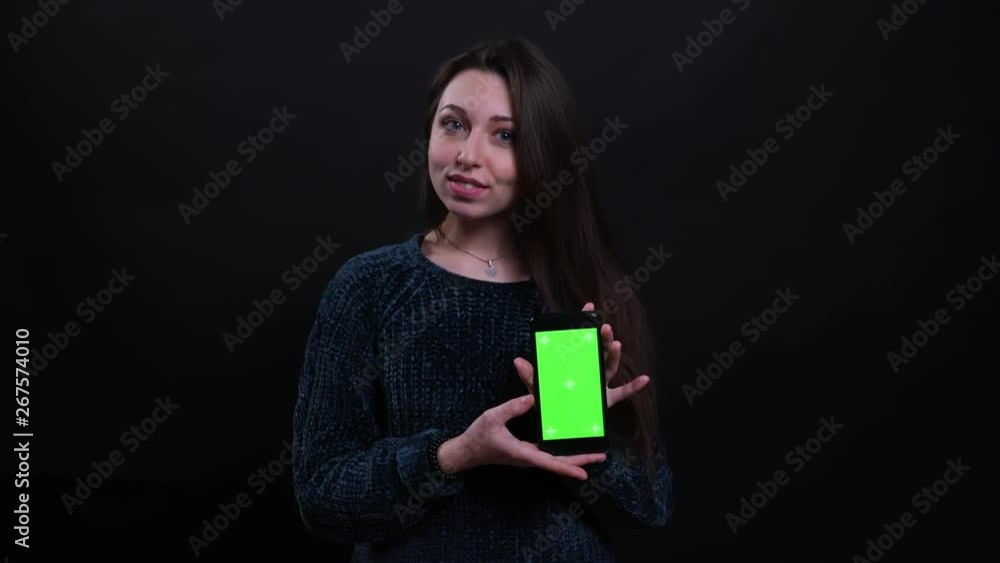 Closeup portrait of adult beautiful caucasian brunette female using phone and showing green screen to camera with background isolated on black Closeup portrait of adult beautiful caucasian brunette female using phone and showing green screen to camera with background isolated on black