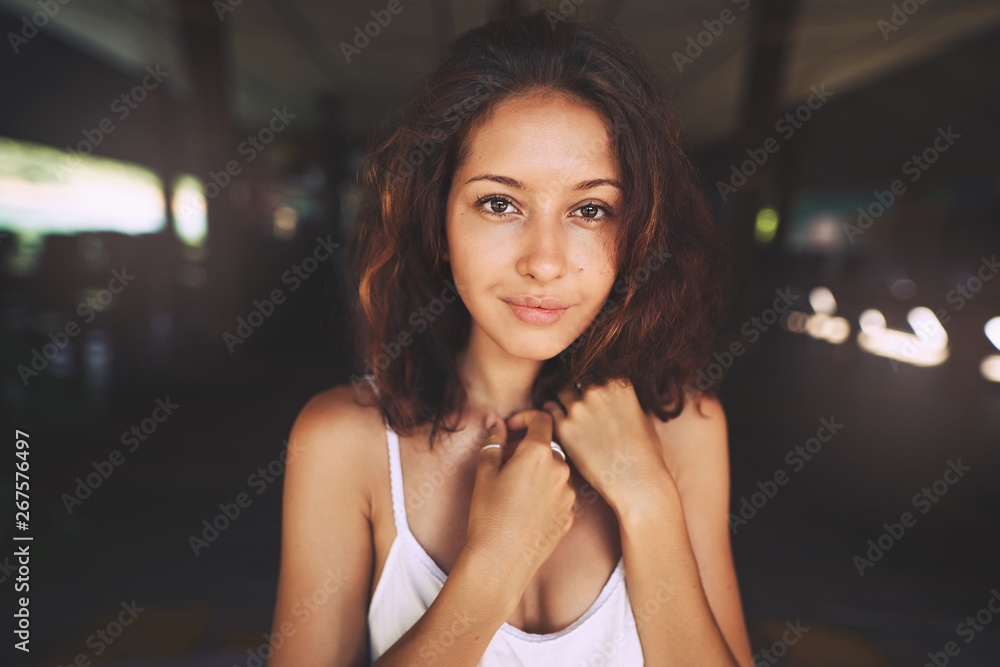 A beautiful girl in a white dress shy looks to camera, in nature light