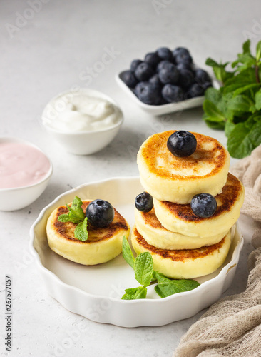 Cottage cheese fritters (syrniki) with fresh blueberries, mint and sauce. Light grey background. Healthy breakfast or diet lunch. Copy space.