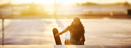 Rear view of young woman sitting with skateboard on steps at park during sunset panorama