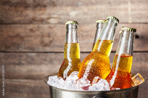 Cold bottles of beer in the bucket on the wooden background photo